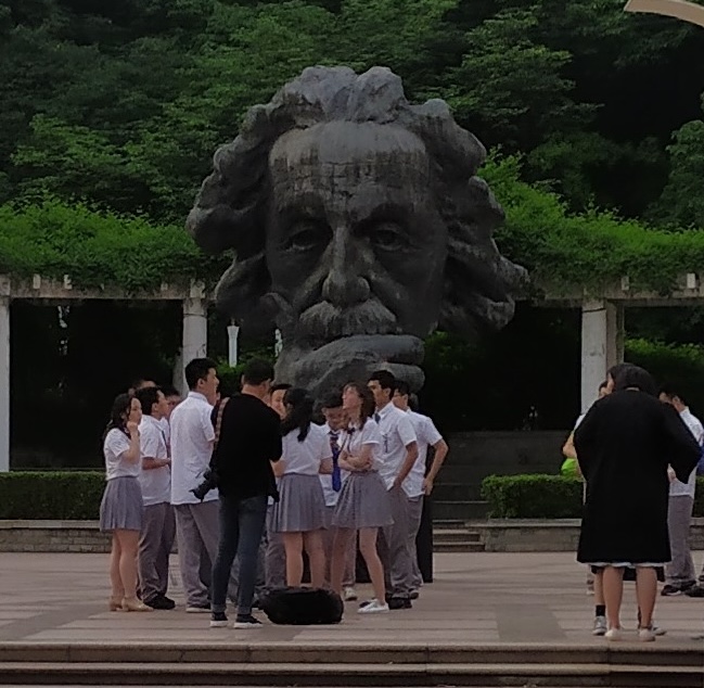 This photo depicts a group of Chinese students on the campus of HUST in Wuhan, China. They are gathering under a large bust of Albert Einstein in 2019.