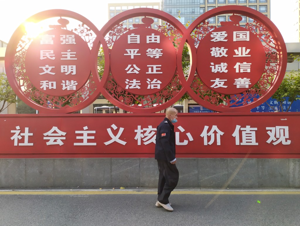 This picture depicts a man walking under a street statue portraying the 12 "socialist core values" of New China.