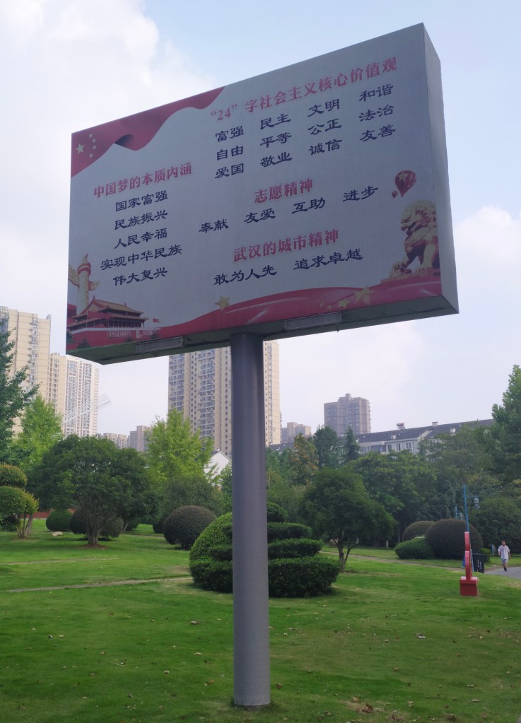 This photo shows a large metal propaganda sign in a park that displays the Socialist Core Values. The photo was taken in 2020 in Wuhan, China.