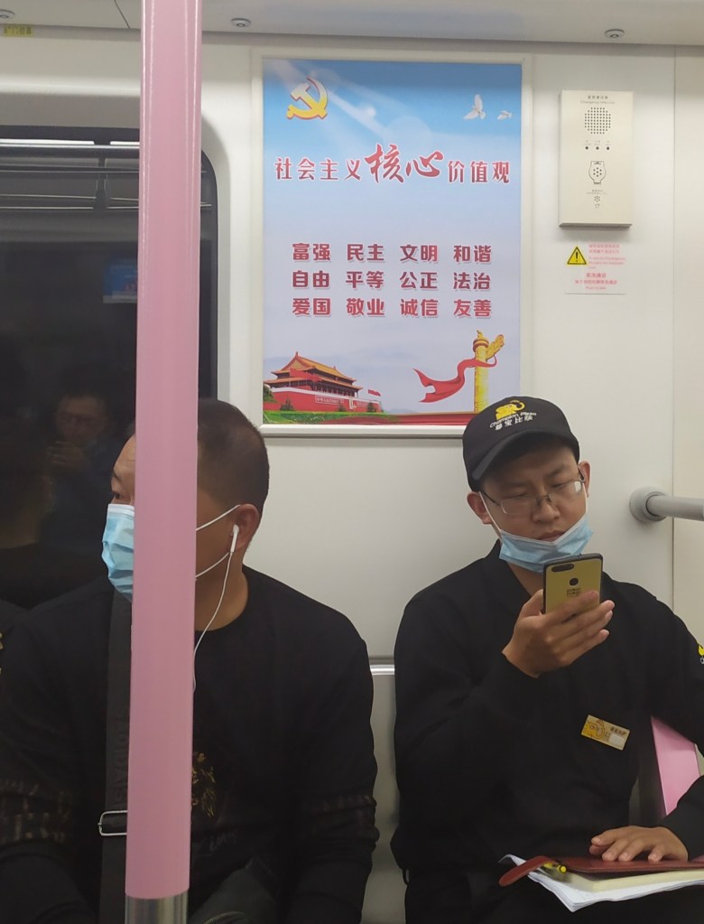 This photo depicts two men sitting on a Wuhan city subway car under a CCP propaganda poster. 