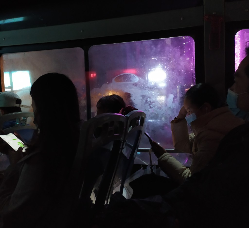 This photo shows people riding the bus in China in 2020. Neon lights and cell phones.