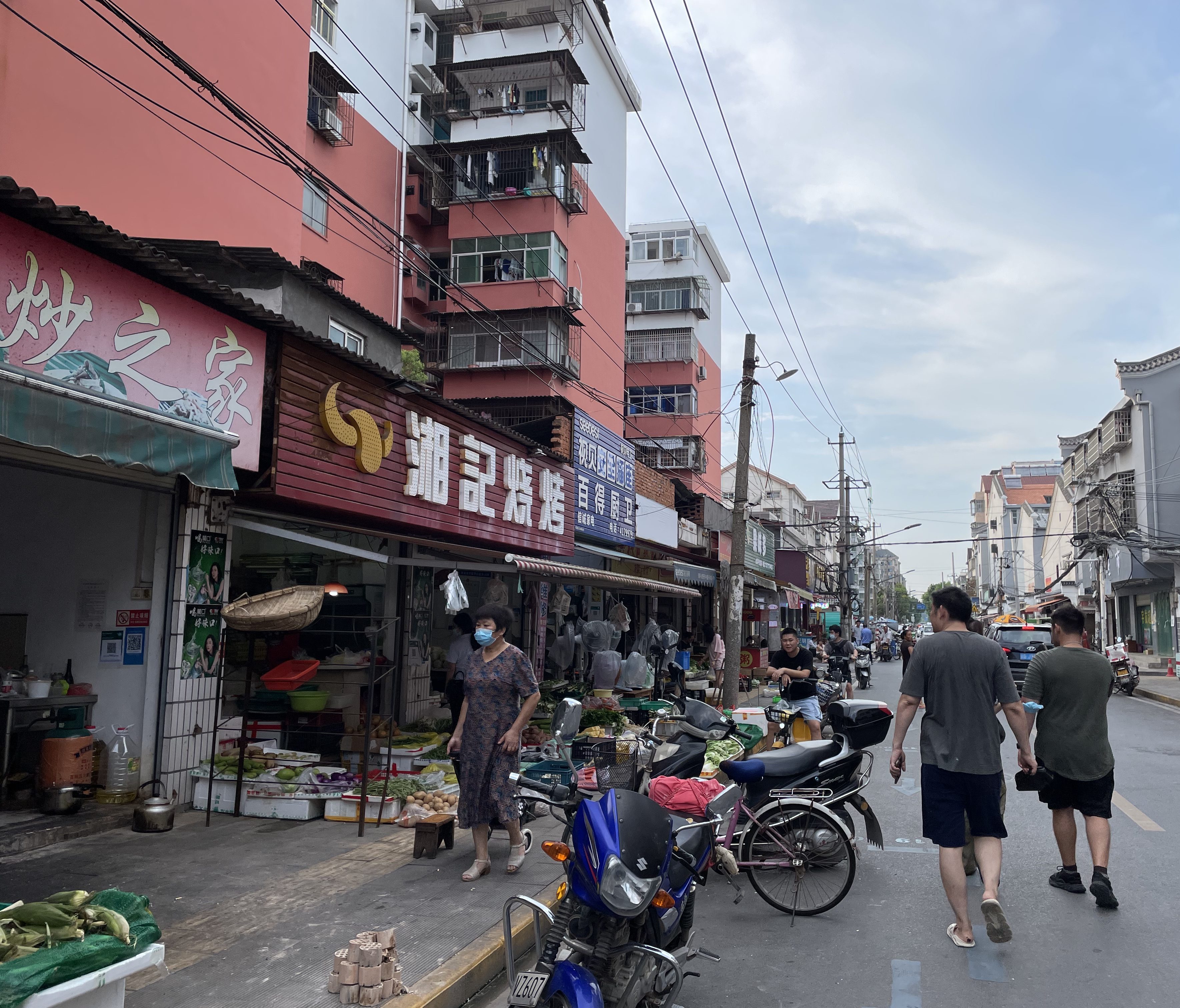 A photo of a busy street in Jingzhou, China in 2021. People are selling vegetables and meat along the side of the road.