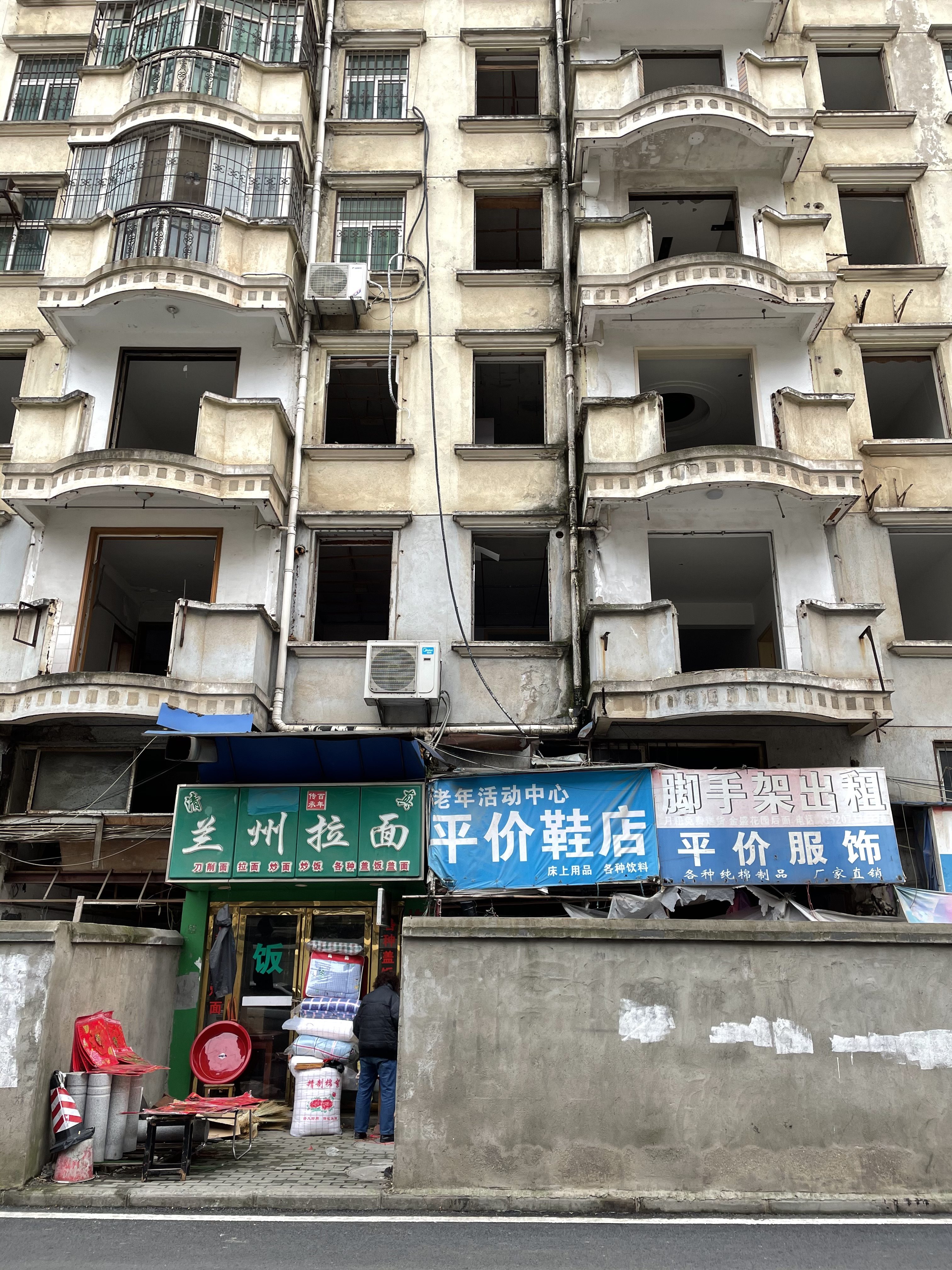 This is a photo of a half-abandoned residential building in Wuhan, it still has some people living in it and some shops operating at the bottom. 2021.