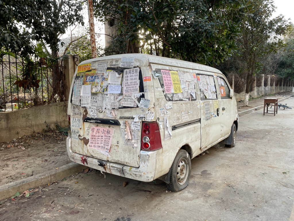 This is a photo of an abandoned van in Wuhan. The van is covered in advertisements. 2021.